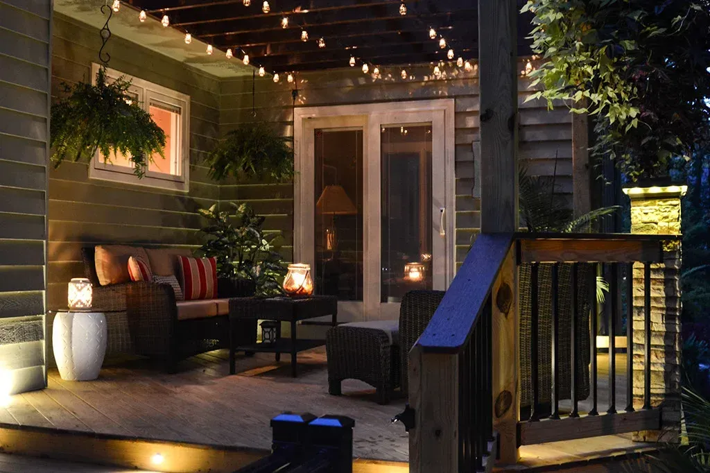 Cozy outdoor patio at night with string lights, seating, plants, and lanterns.