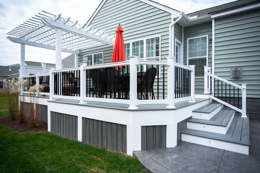 White deck with black railings, a pergola, and an orange umbrella. Gray siding on house.
