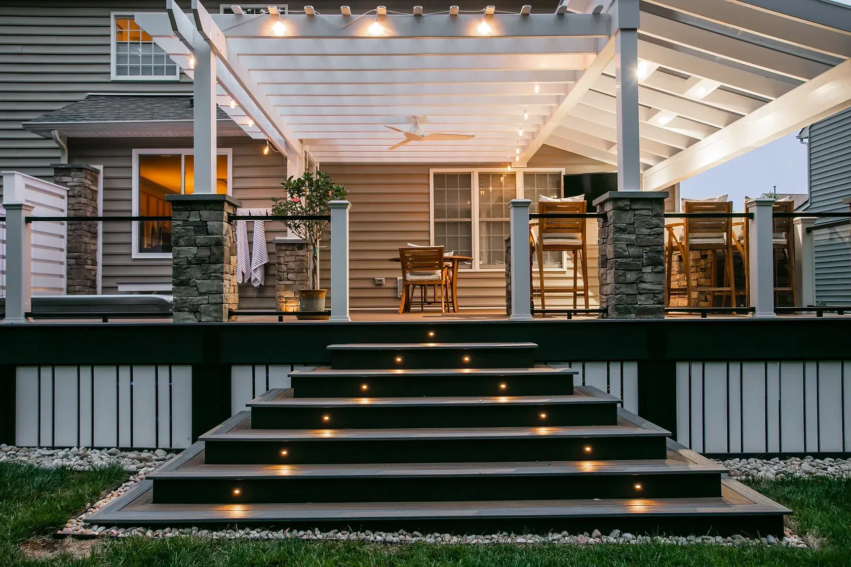 Wooden deck with illuminated steps leading to a seating area under a pergola.