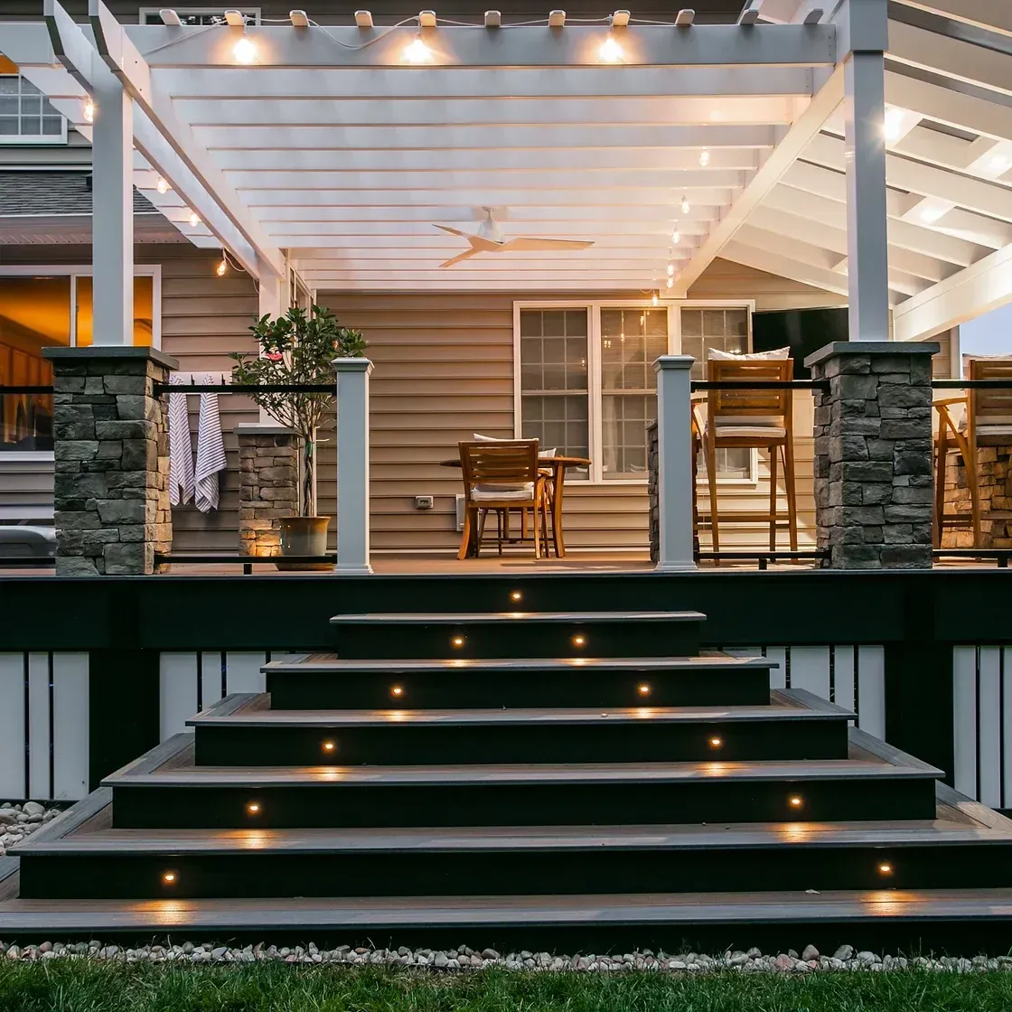 Outdoor deck with steps and pergola, lit by overhead and step lights.