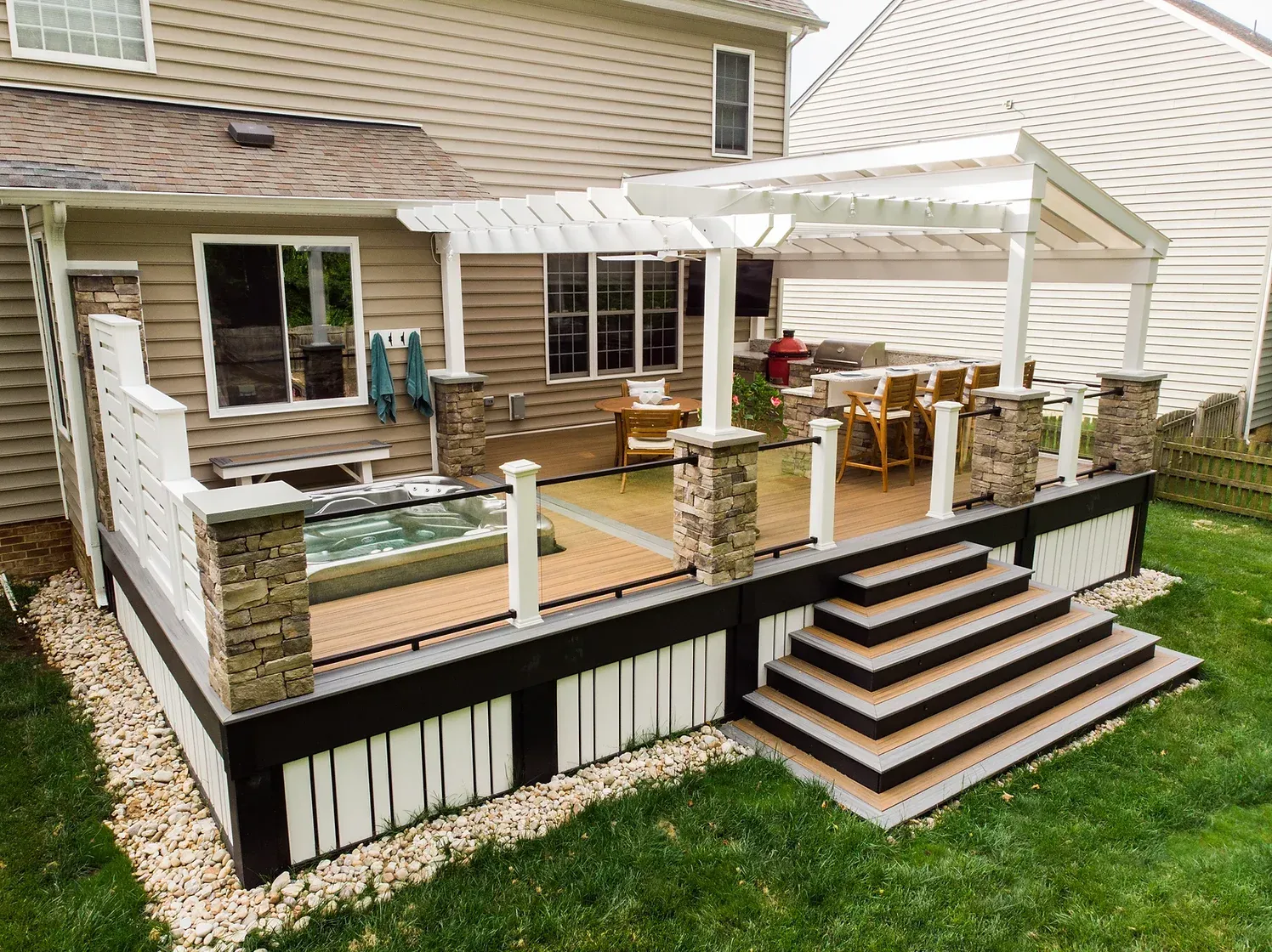 A multi-level backyard deck with a pergola, hot tub, and steps surrounded by a lawn.