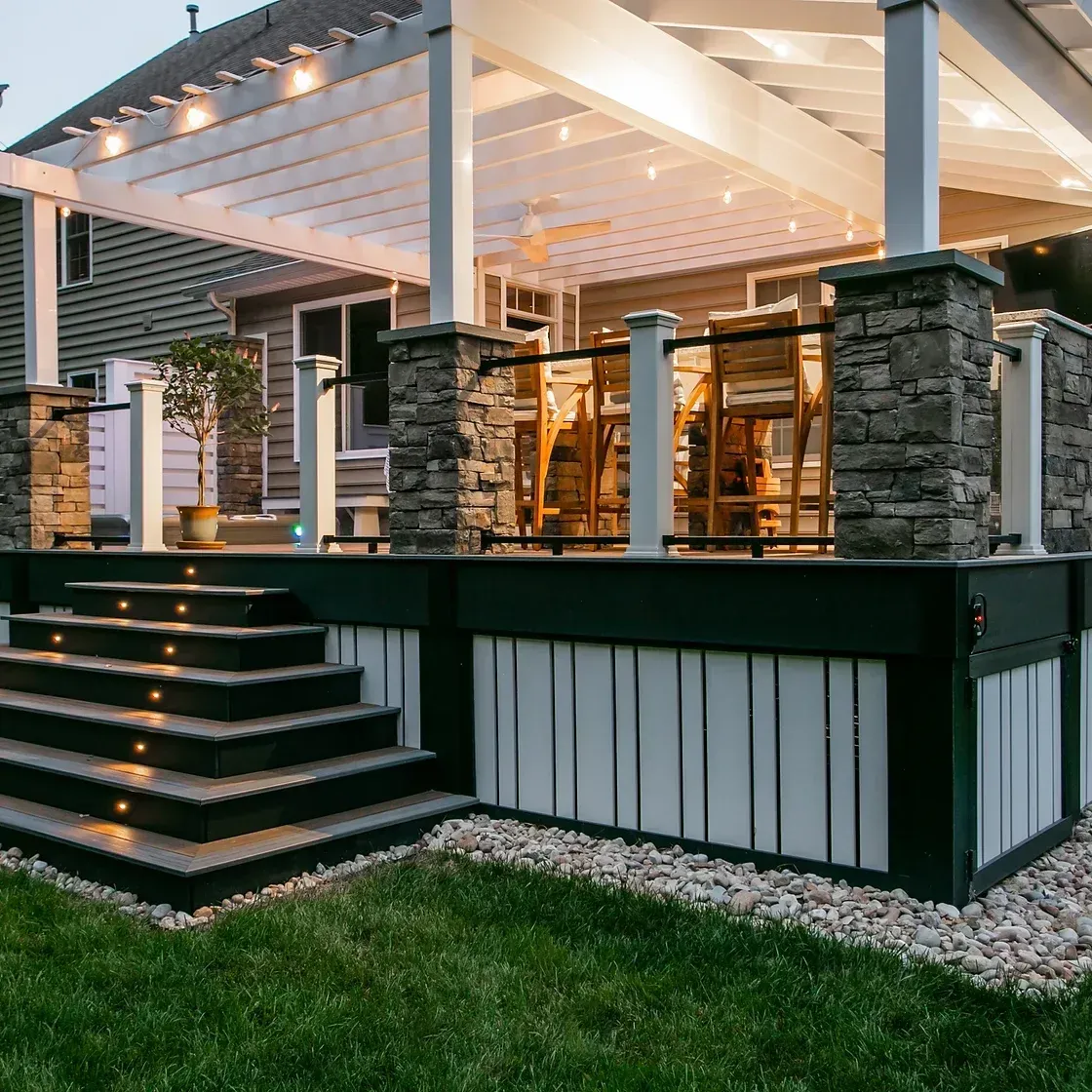 Backyard deck with pergola, stone columns, steps with lighting, and white and black trim.
