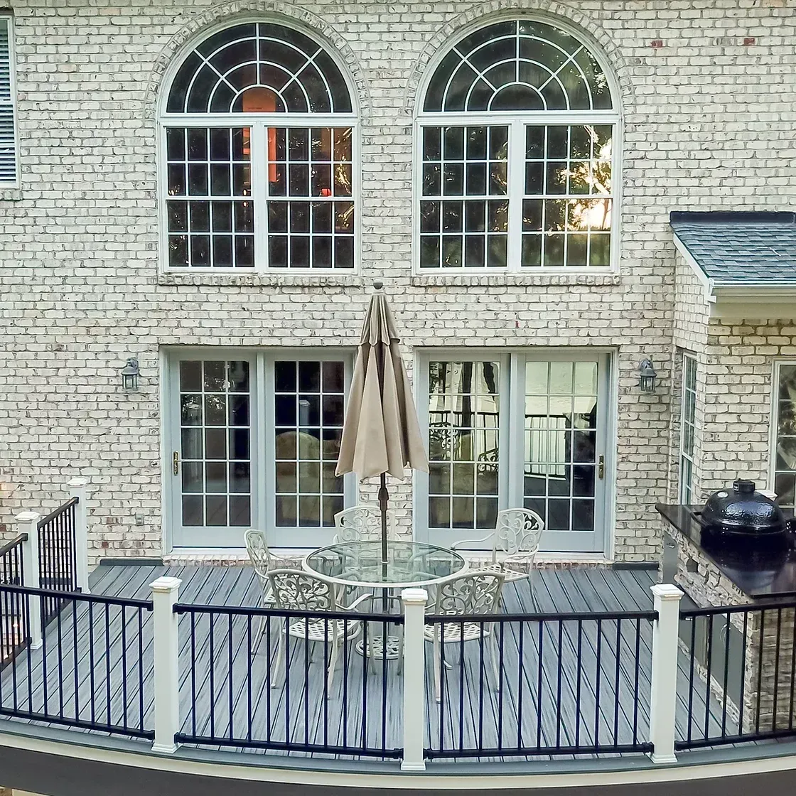 Brick home exterior with deck, two arched windows, two glass doors, and a patio umbrella.