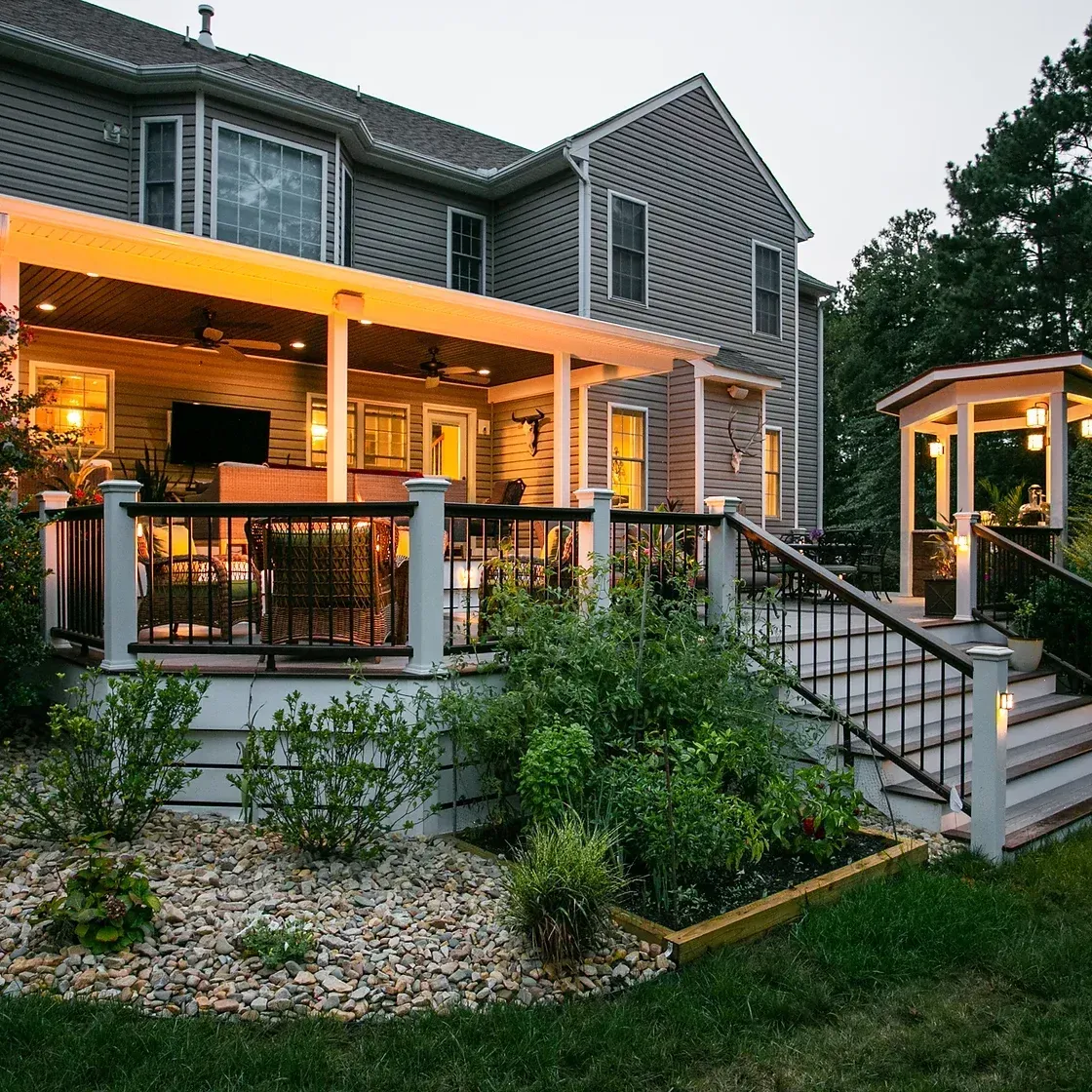 Backyard deck with pergola, gazebo, and house. Evening with warm lighting.
