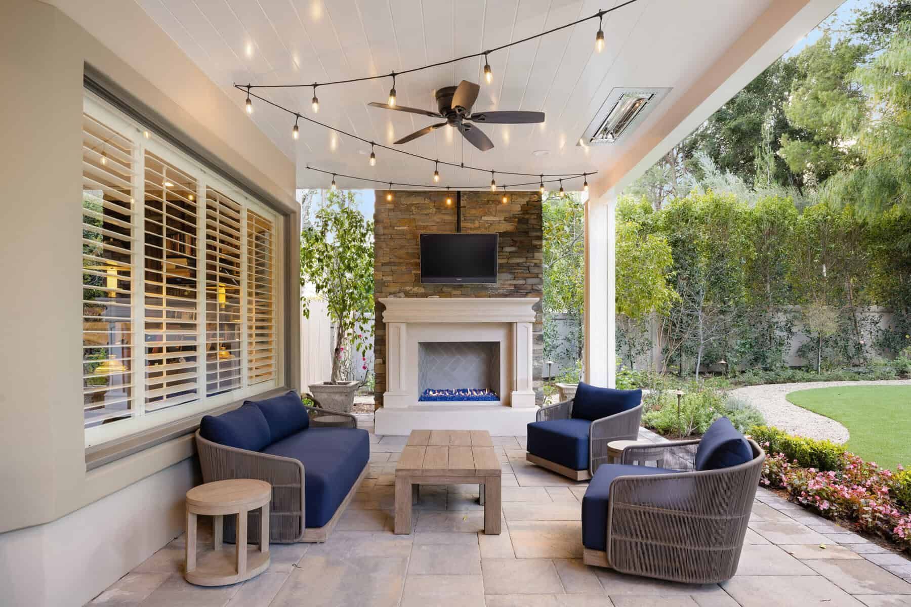 Patio with seating, fireplace, string lights, and a view of a garden.