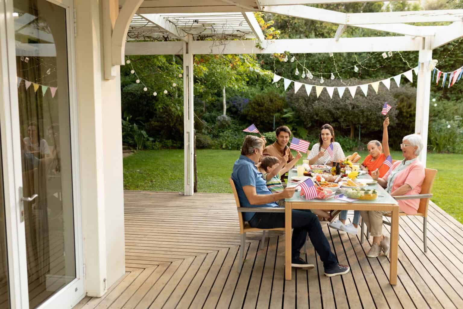 Family celebrating outdoors at a table decorated with flags under a white pergola.