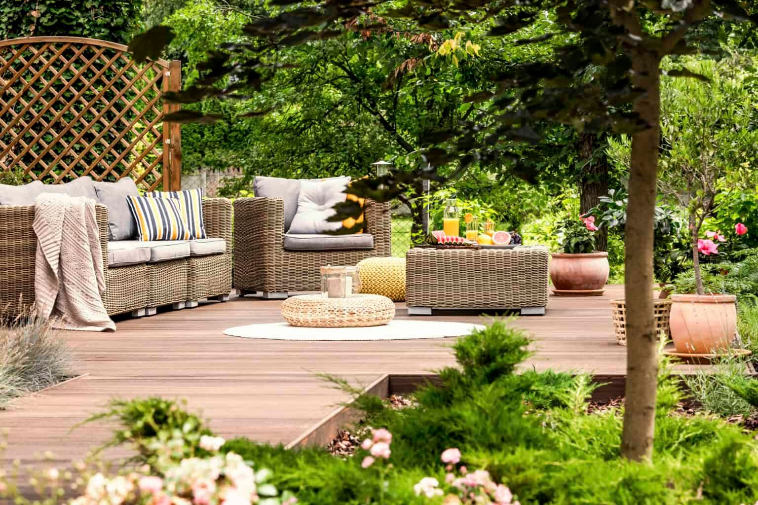 Outdoor patio with wicker furniture, wood deck, and lush greenery.