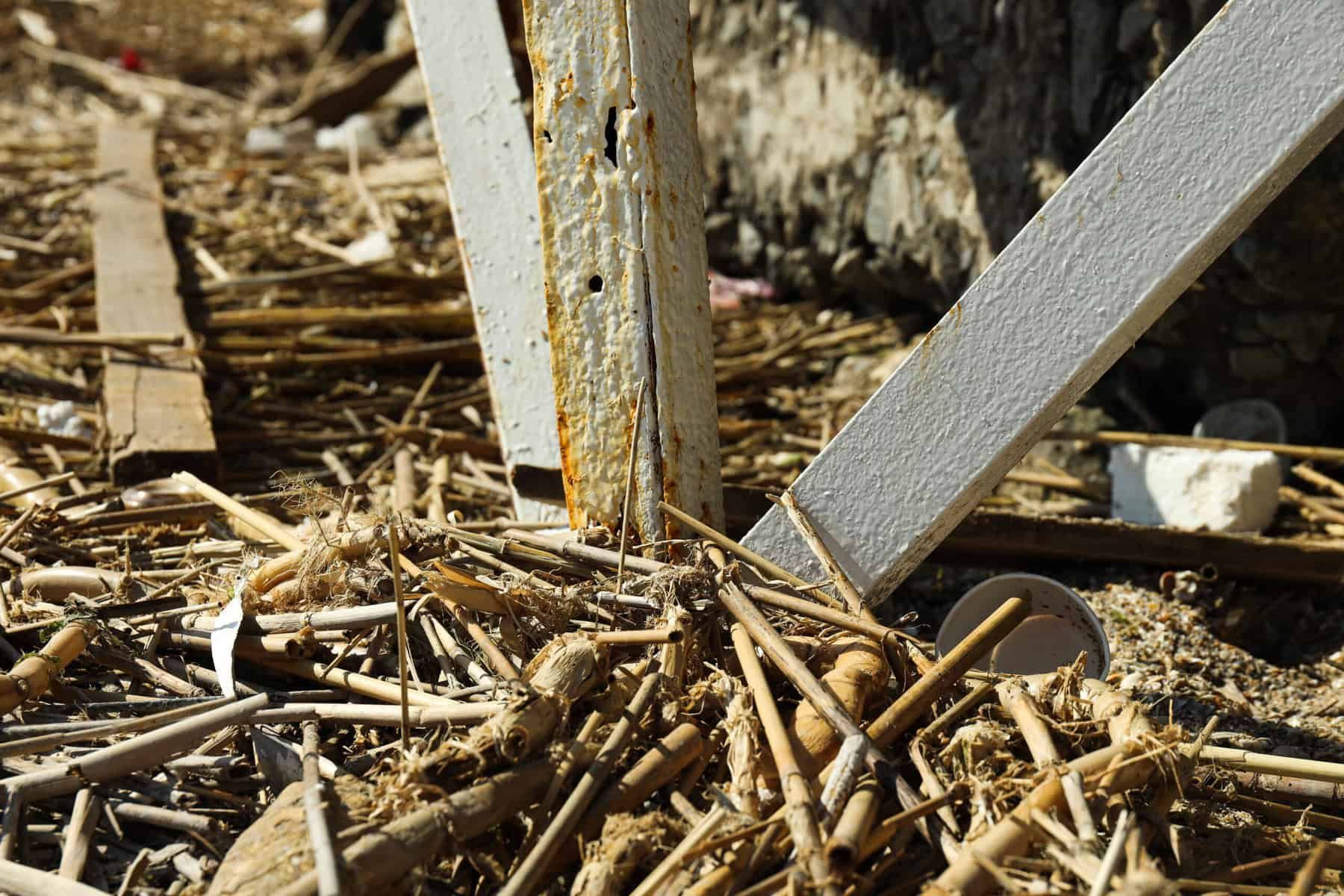 Close-up of weathered wooden and metal support beams amid debris on a sunlit day.