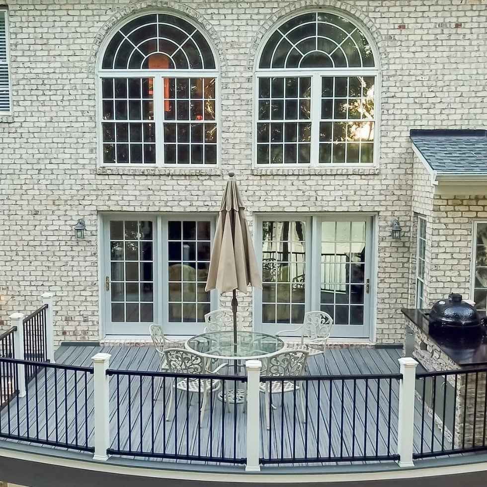 Brick house exterior with deck, arched windows, and patio furniture.