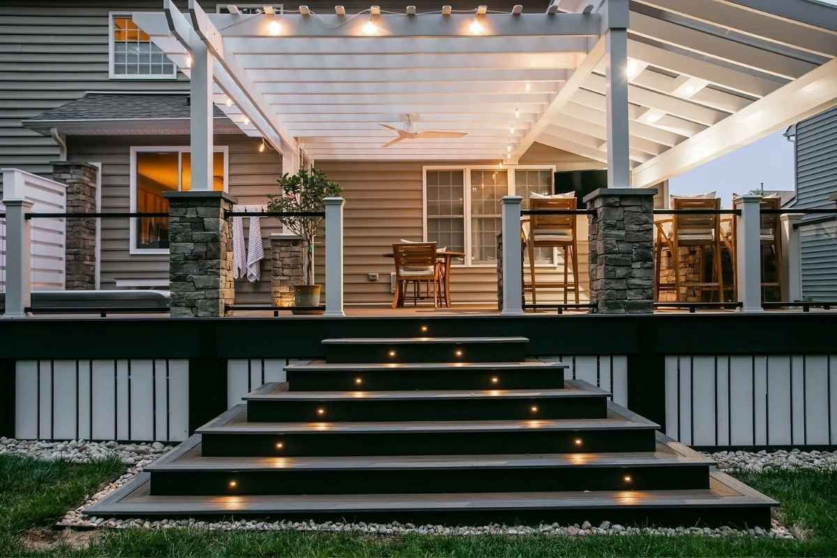 Wooden deck with steps lit by small lights, leading to a covered patio with seating and string lights.