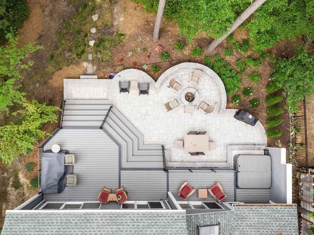 Overhead view of a multi-level outdoor patio with seating, fire pit, hot tub, and deck, surrounded by trees.