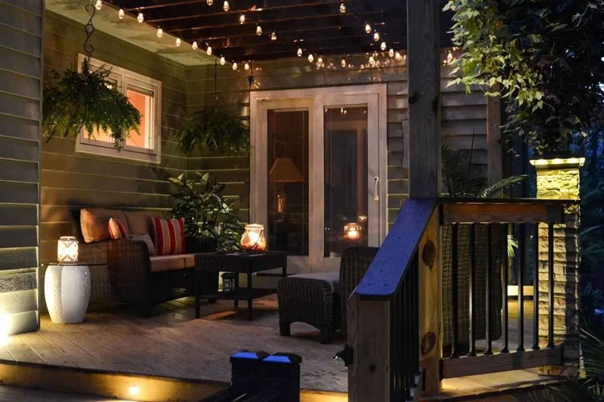 Cozy outdoor patio at night with string lights, seating, plants, and lanterns.