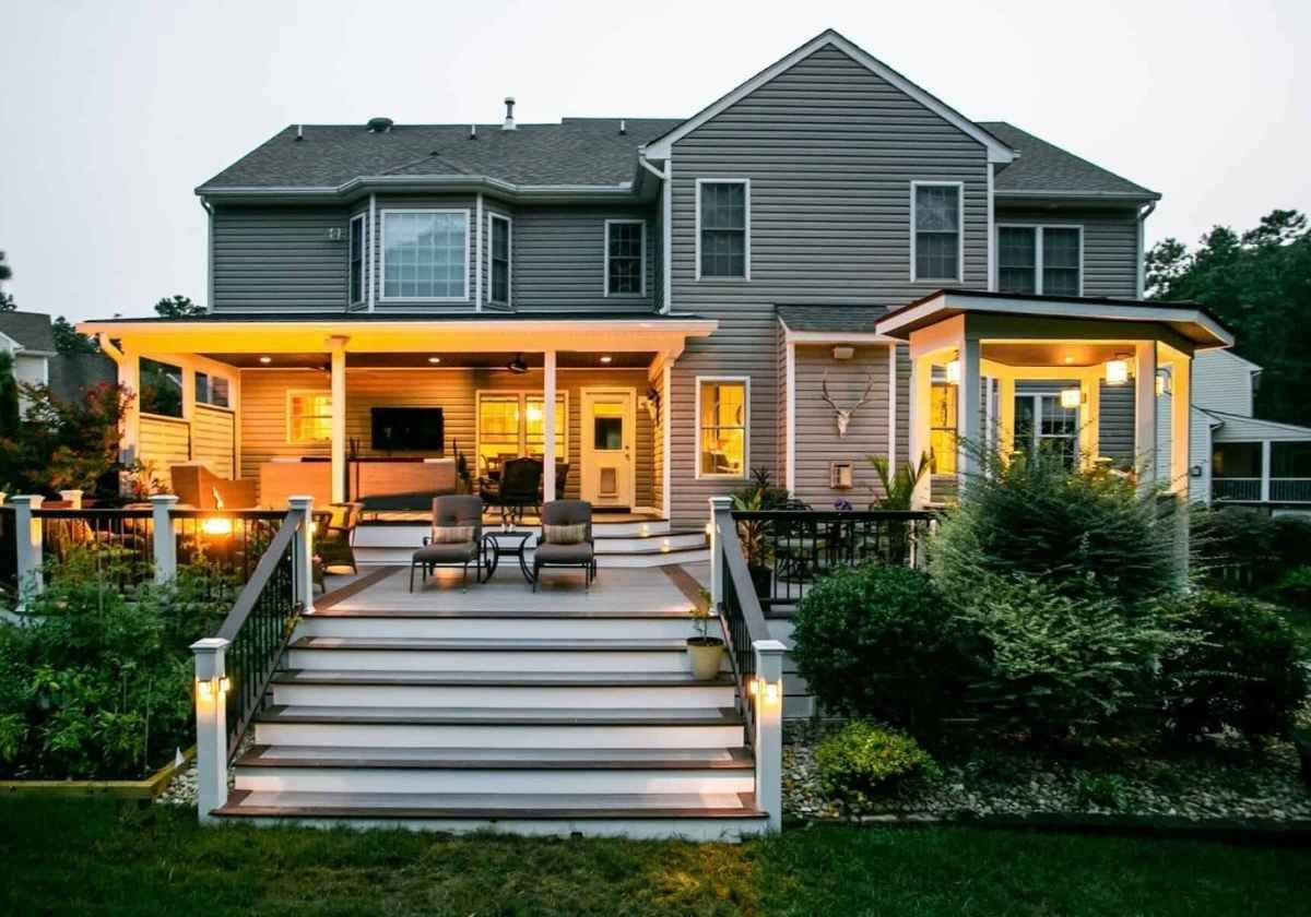Backyard deck of a gray house with seating, lights, and landscaping.