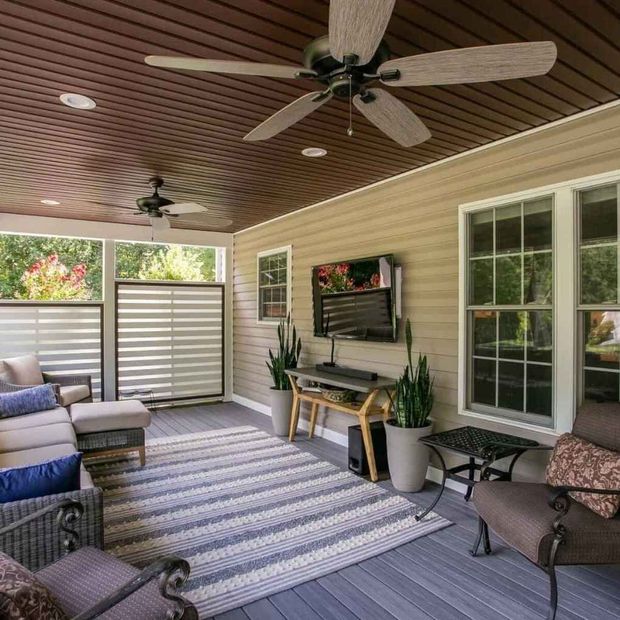 Covered porch with seating, rug, TV, and ceiling fans.