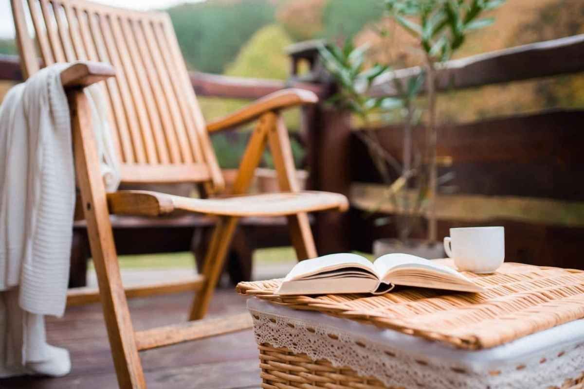 Wooden deck with chair, open book, and coffee cup on wicker table. A white sweater hangs on the chair.