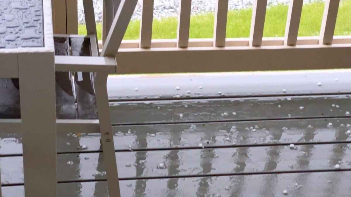 Hail covering a wooden deck, with a railing and partial view of grass.