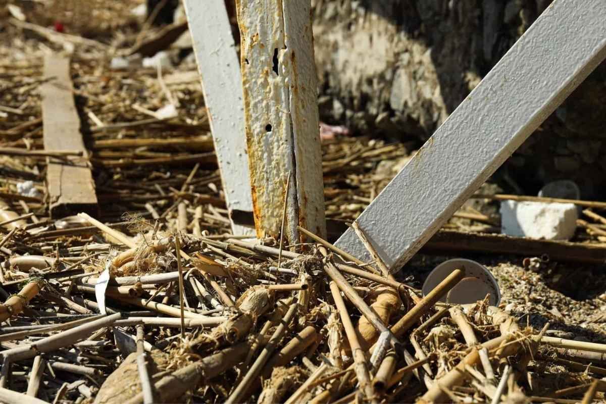 Close-up of weathered metal support beams amid debris and dried vegetation.