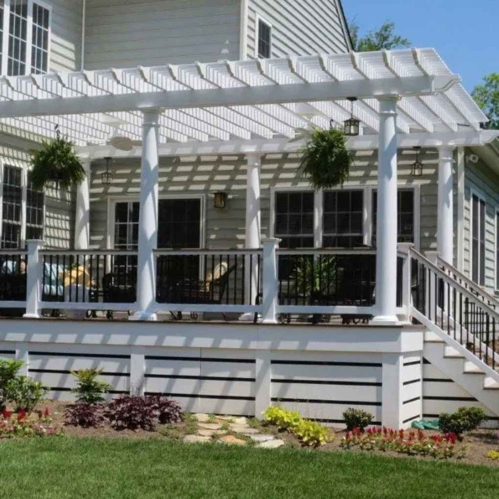 White pergola over a deck with hanging plants, stairs, and a house in the background.