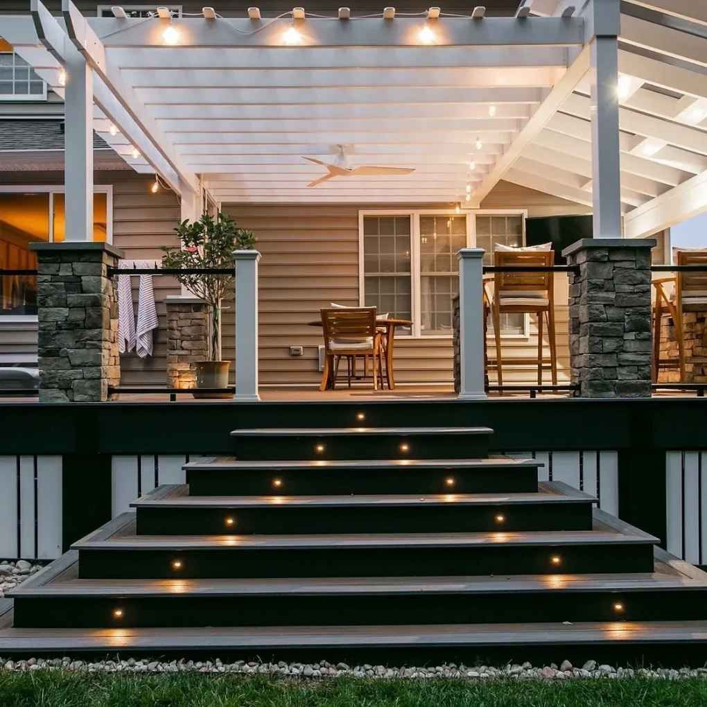 Outdoor deck with steps and pergola, lit by overhead and step lights.