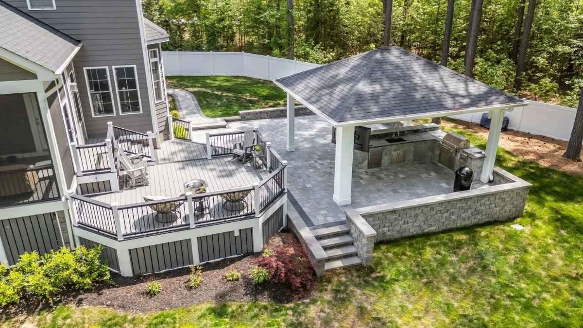 An elevated wooden deck with a hot tub and pergola, accessible by steps, next to a house with a green lawn.