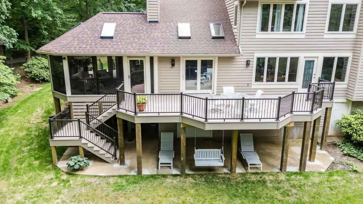 Backyard deck with fire pit and screened porch attached to a light blue house with a gray roof.