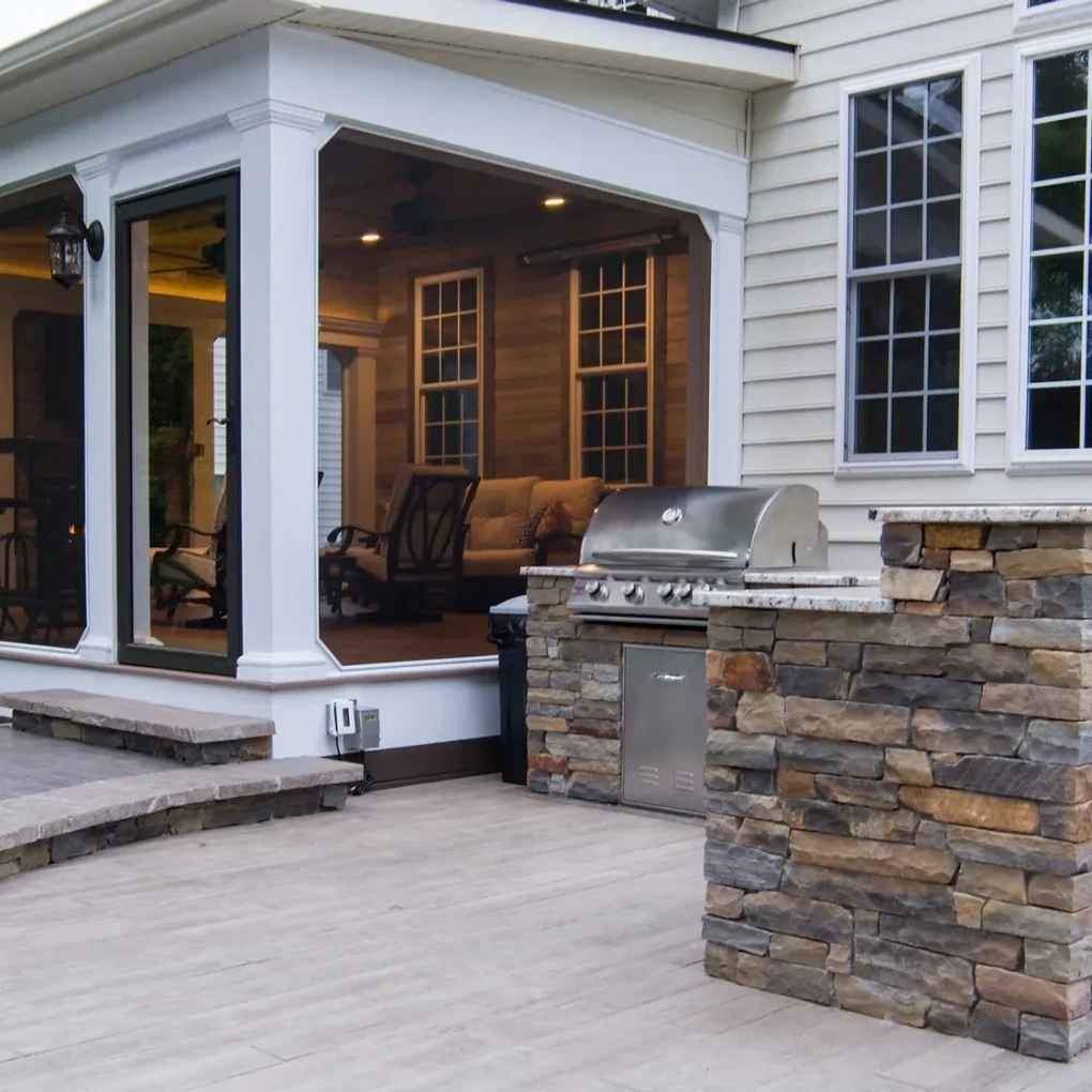 Backyard patio with built-in grill, seating area under covered porch with wood siding, and stone accents.