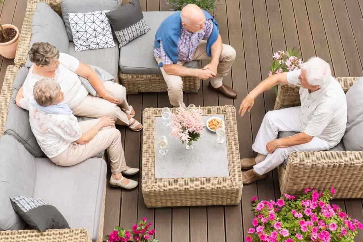 Group of people seated on outdoor wicker furniture, socializing around a table with snacks and flowers.