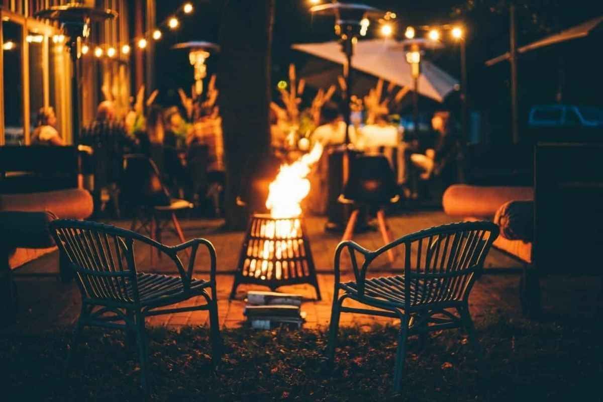 Two chairs face a fire pit in a cozy outdoor setting with string lights and heaters.