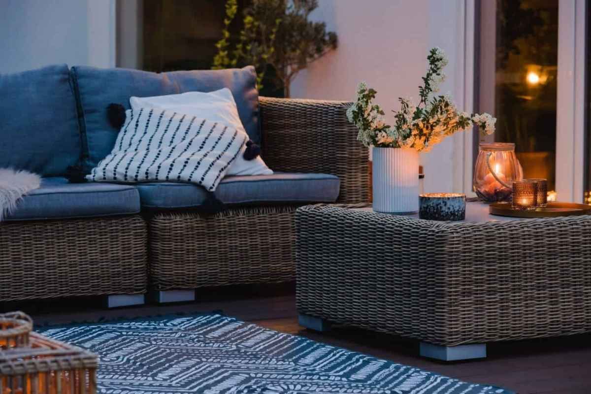 Wicker patio furniture with blue cushions, coffee table with candles, and rug on a patio at dusk.
