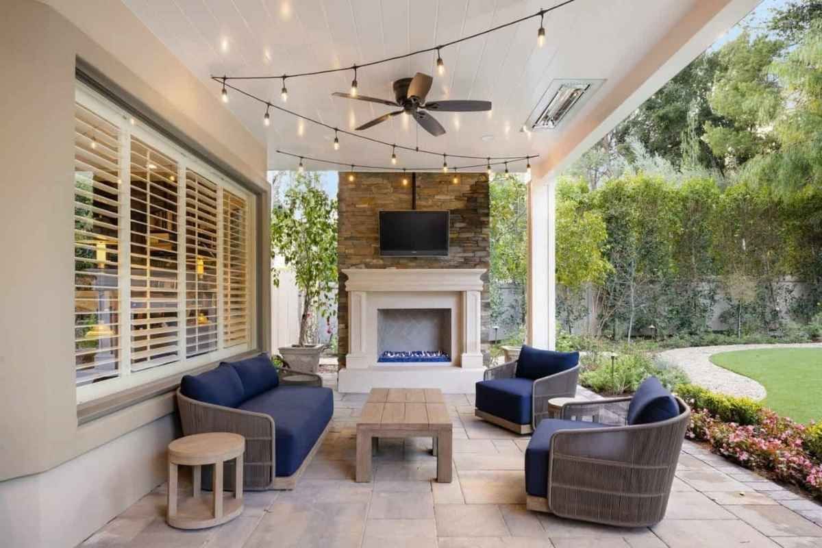 Patio with blue seating, fireplace, TV, and string lights, overlooking a garden.