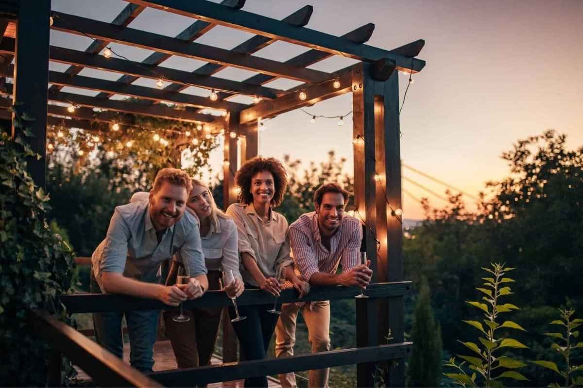 Friends gathered under a pergola with string lights, smiling at sunset.