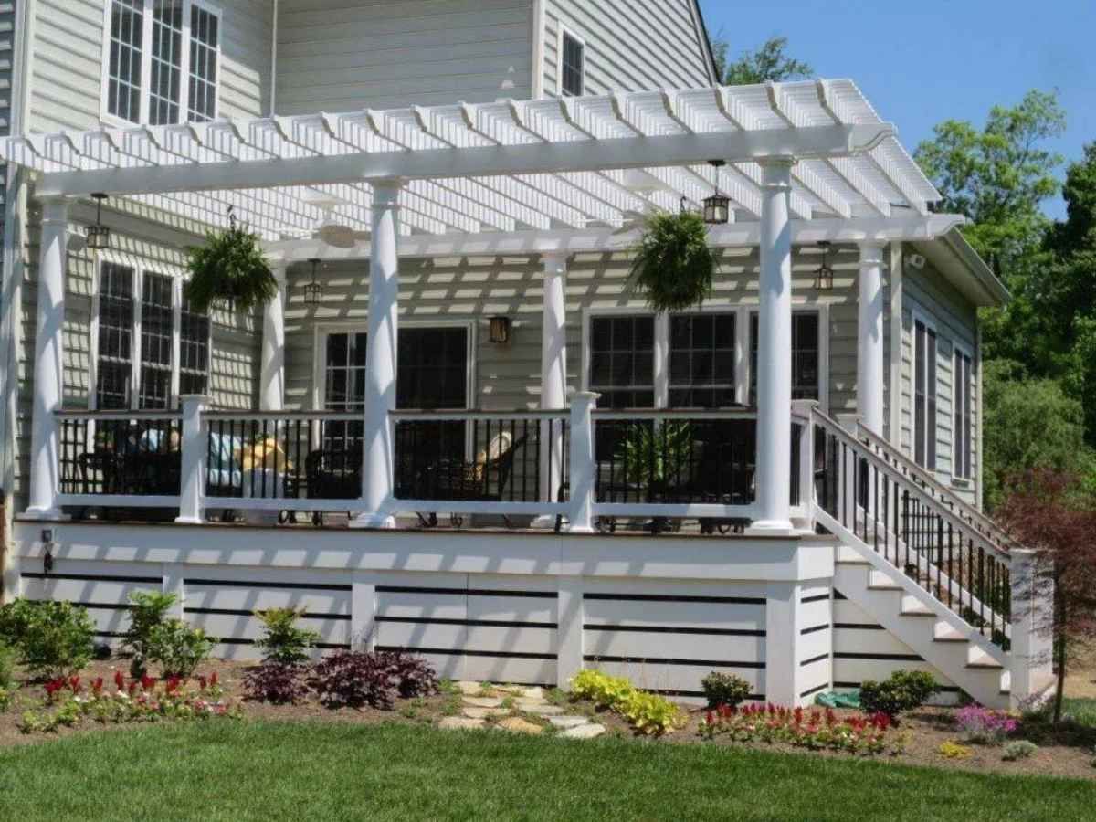 White pergola over a raised deck with steps, a black railing, and potted plants.
