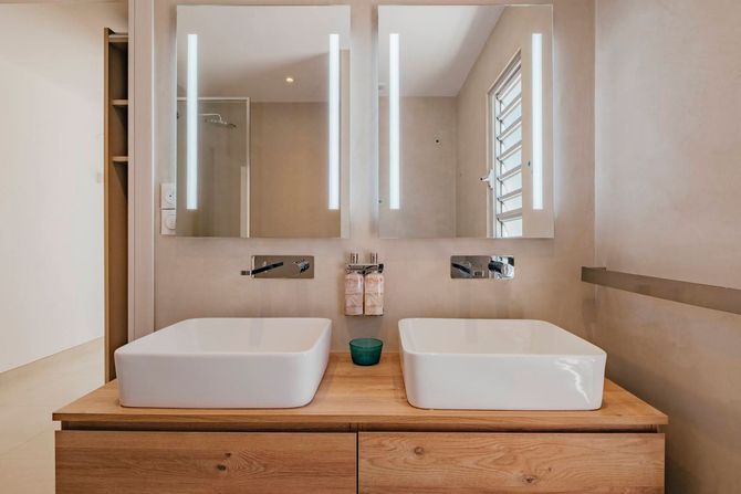 Modern bathroom with a bathtub, two sinks, and a door leading to a patio with greenery.