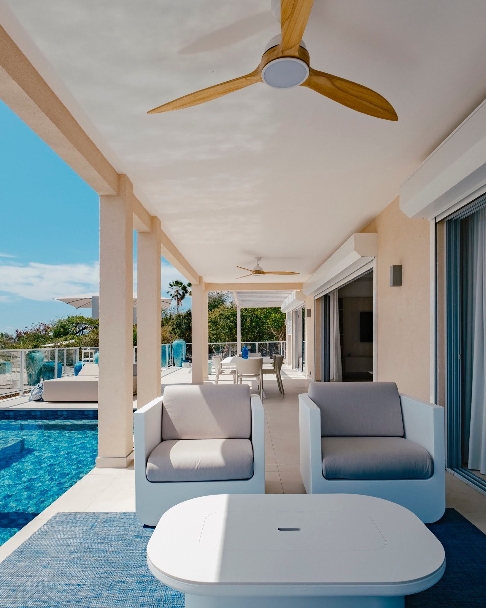 A pool overlooks a tropical ocean view from a porch, with palm trees and a parasol.