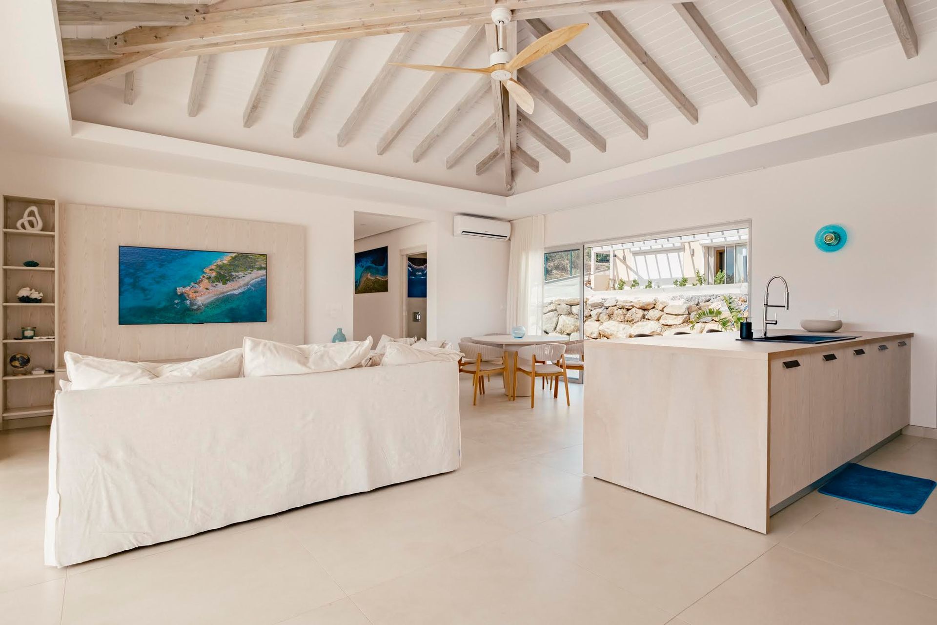 Living room with pale peach walls, vaulted ceiling, large windows overlooking a pool and ocean.