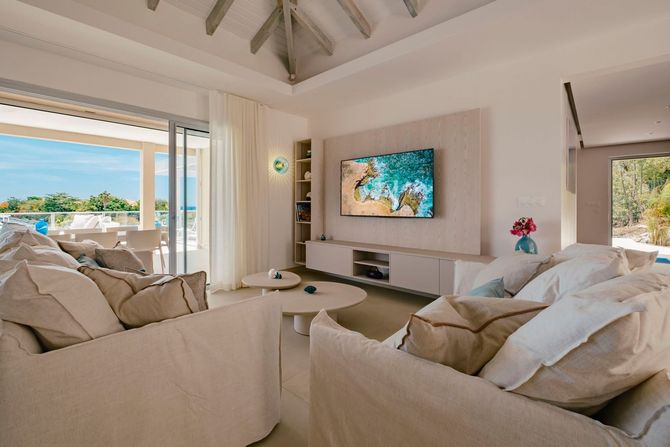 Living room with cream-colored sofas, white beams, and a large TV.