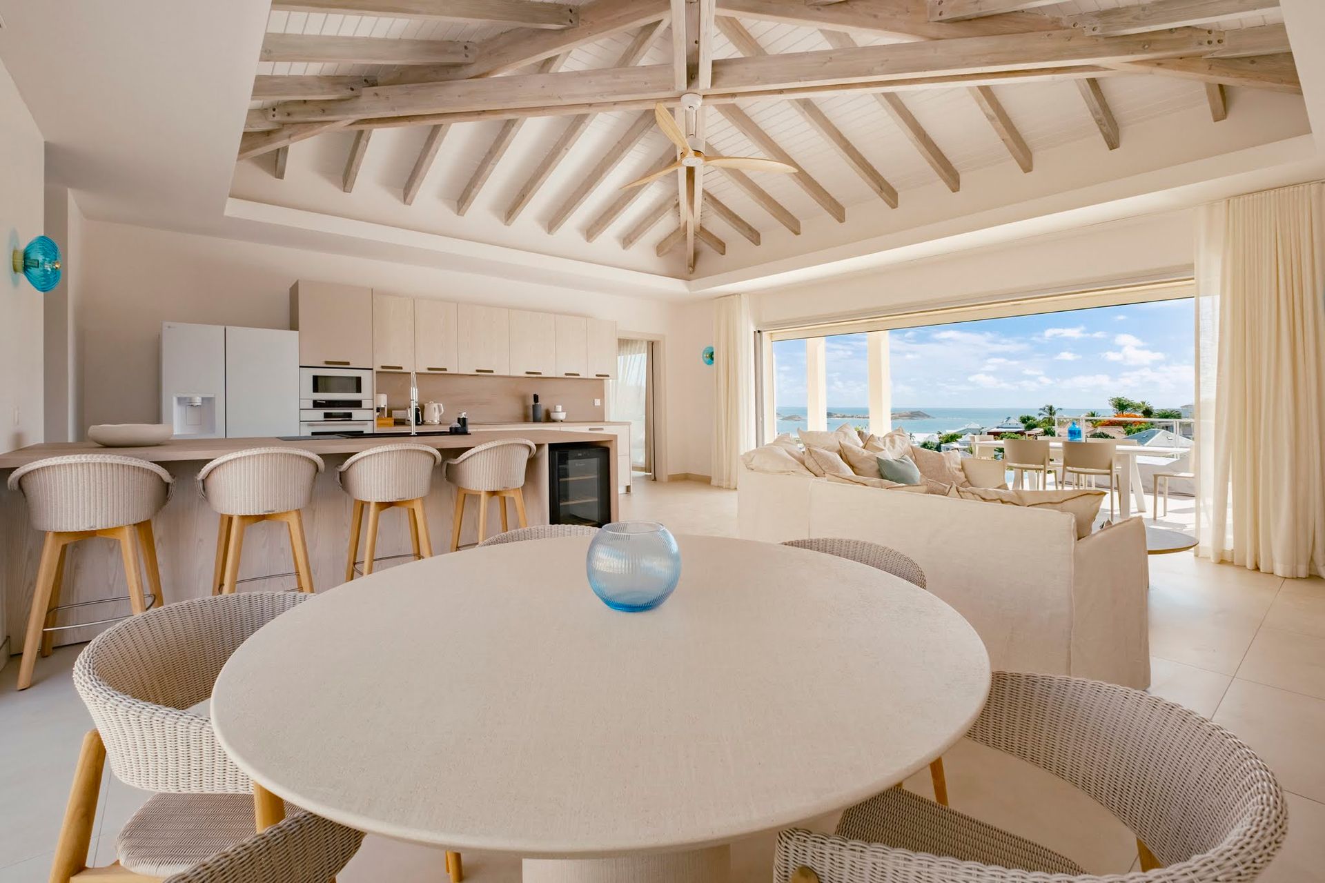 Open-concept living space with a kitchen and seating area, pale beige tones, and a view of the ocean.