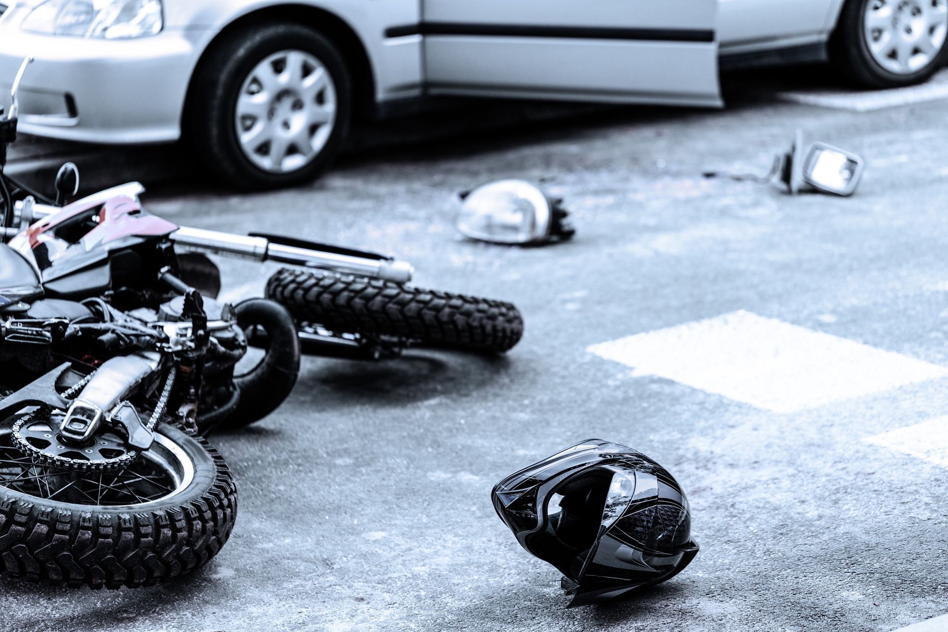A fallen motorcycle, a helmet, and scattered debris on a road near a silver car, suggesting a traffic accident.