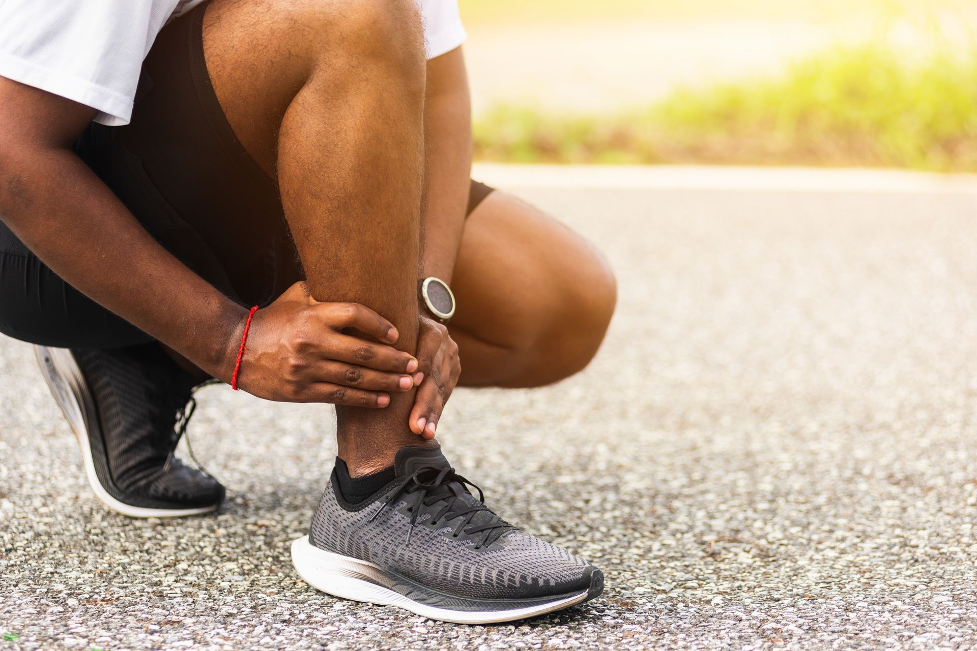 A person kneeling on a paved surface, holding their lower leg while experiencing a suspected running-related injury.