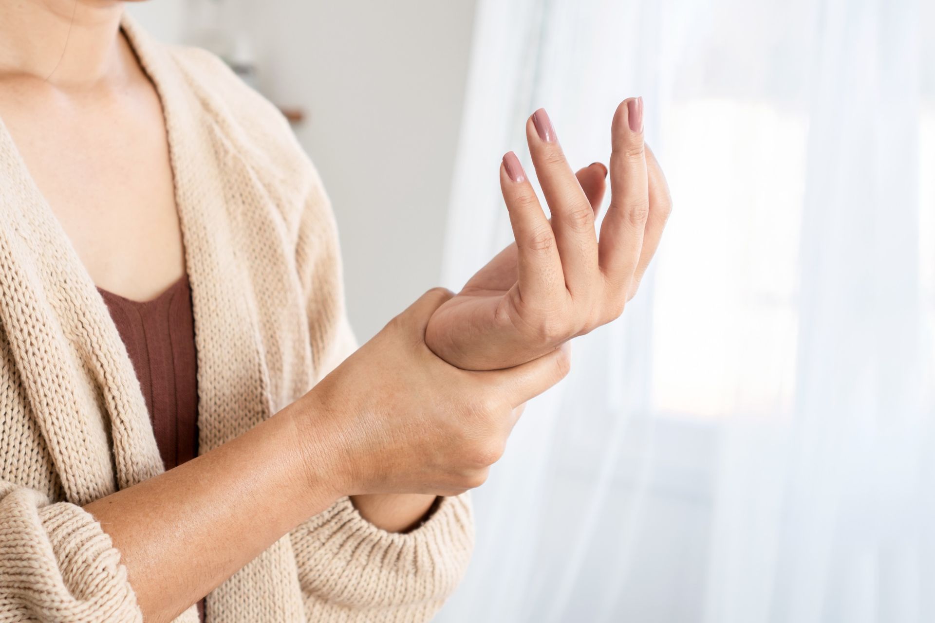 A person in a beige sweater holding their wrist with their other hand, suggesting pain or discomfort.