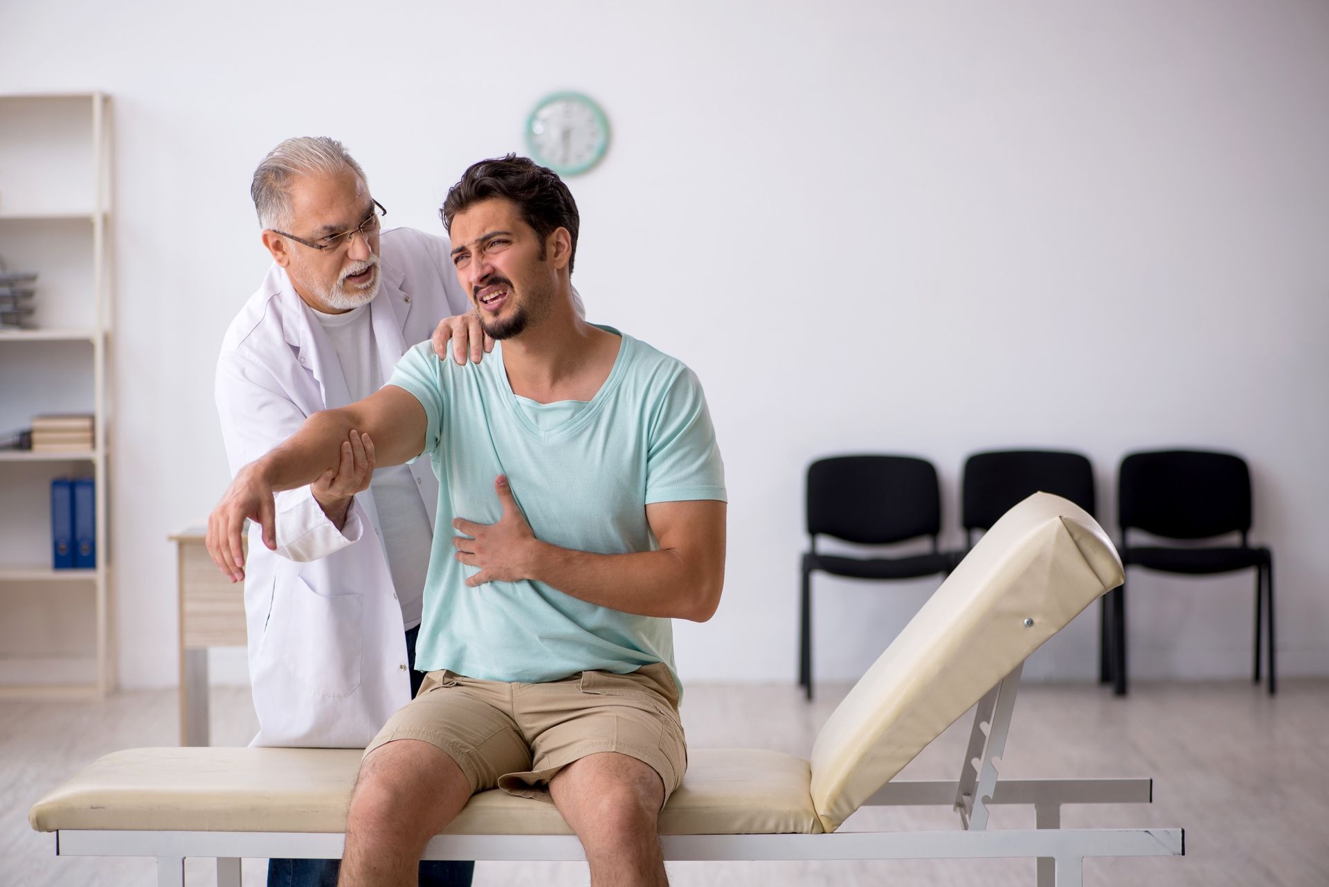 A doctor in a white coat examines a patient's injured arm in an office setting.