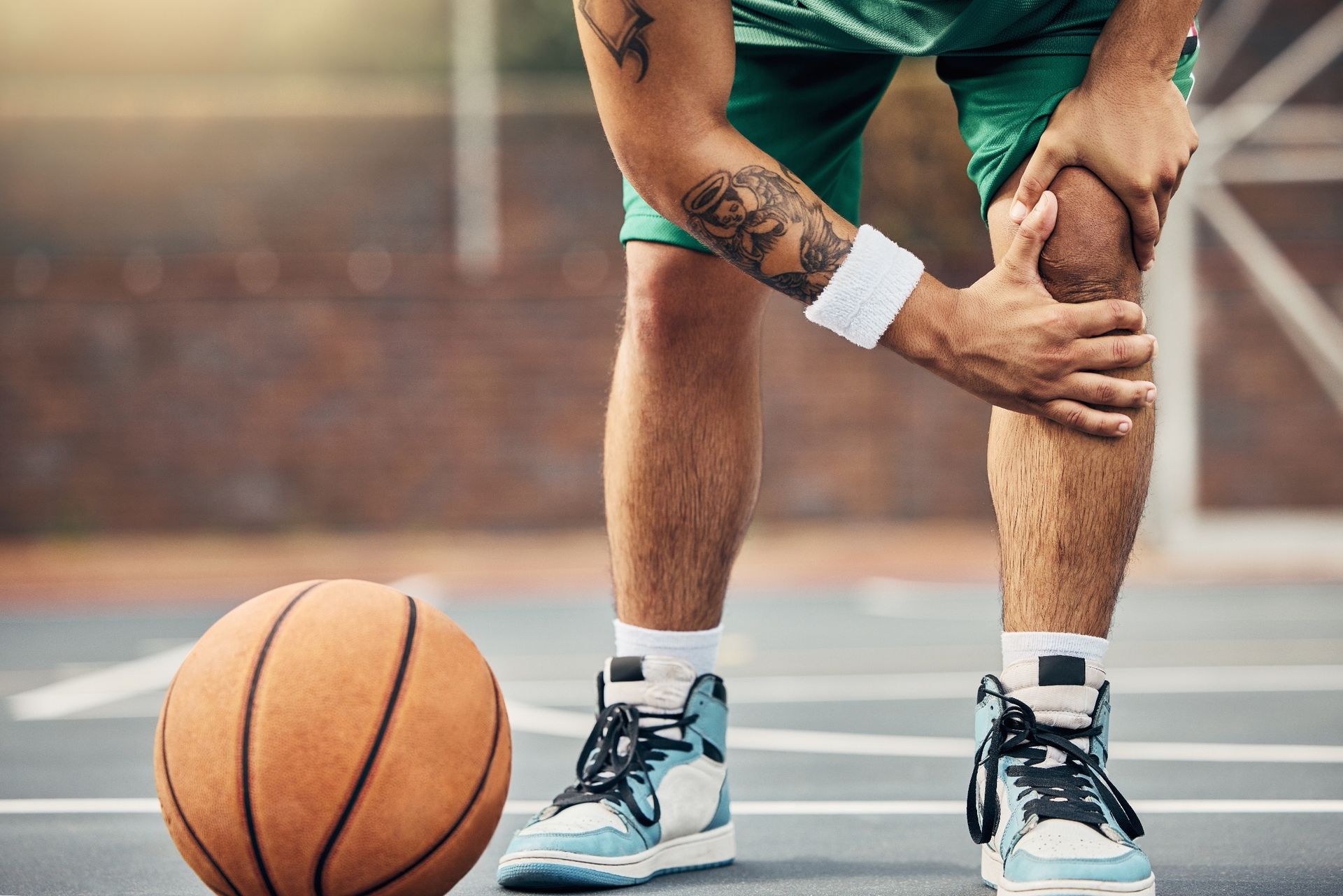 A basketball player holding their knee in pain on an outdoor court, with a basketball nearby.