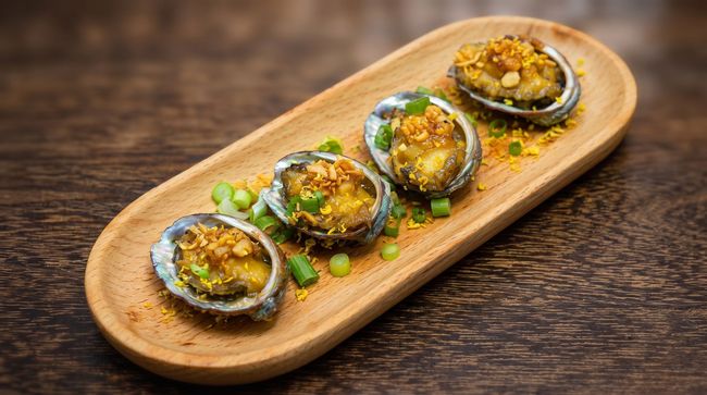 Four baked shellfish topped with sauce on a wooden serving board