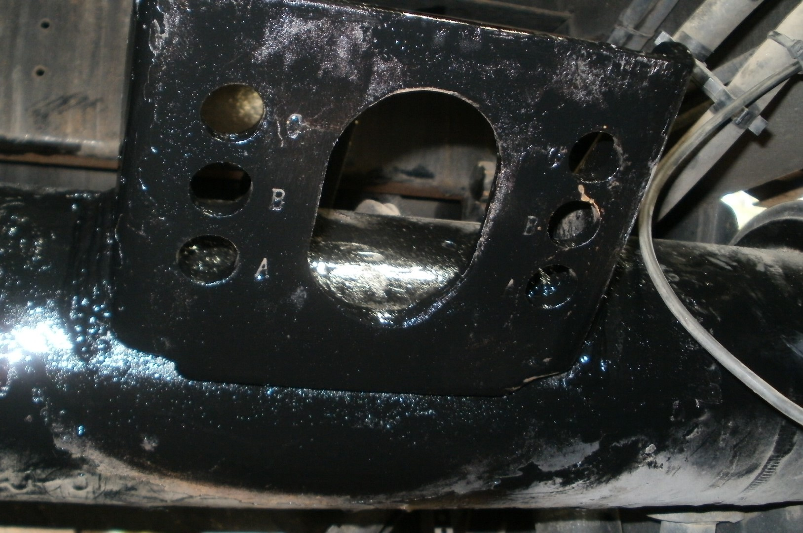 Black metal bracket attached to a cylindrical component. It has holes and a large opening.