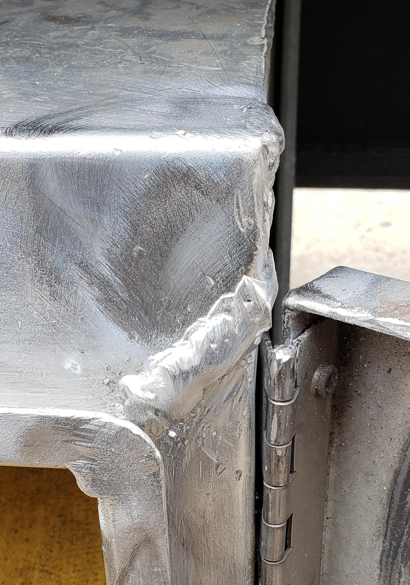 Close-up of a metal box with a welded joint near an open hinge.