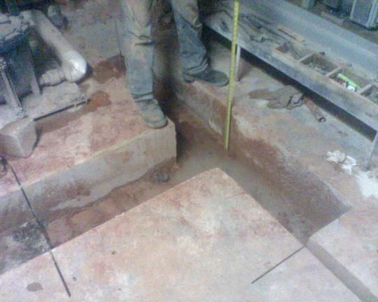 A man is standing next to a large circular saw cutting a concrete surface.