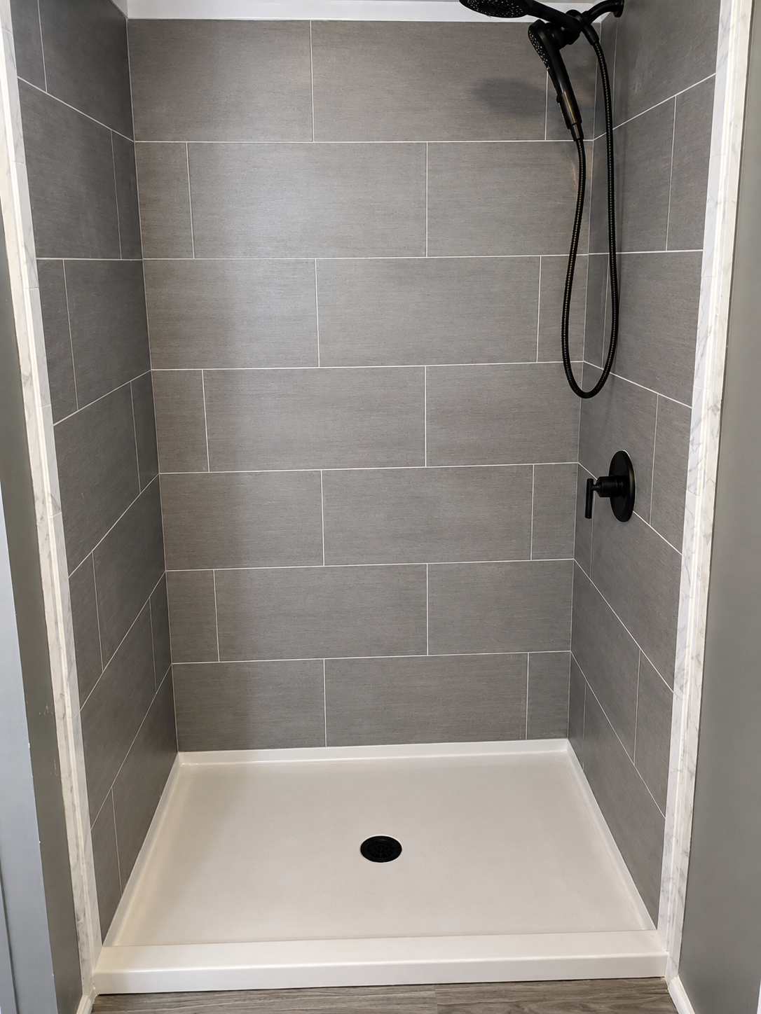 Empty gray-tiled shower with white base and black showerhead.
