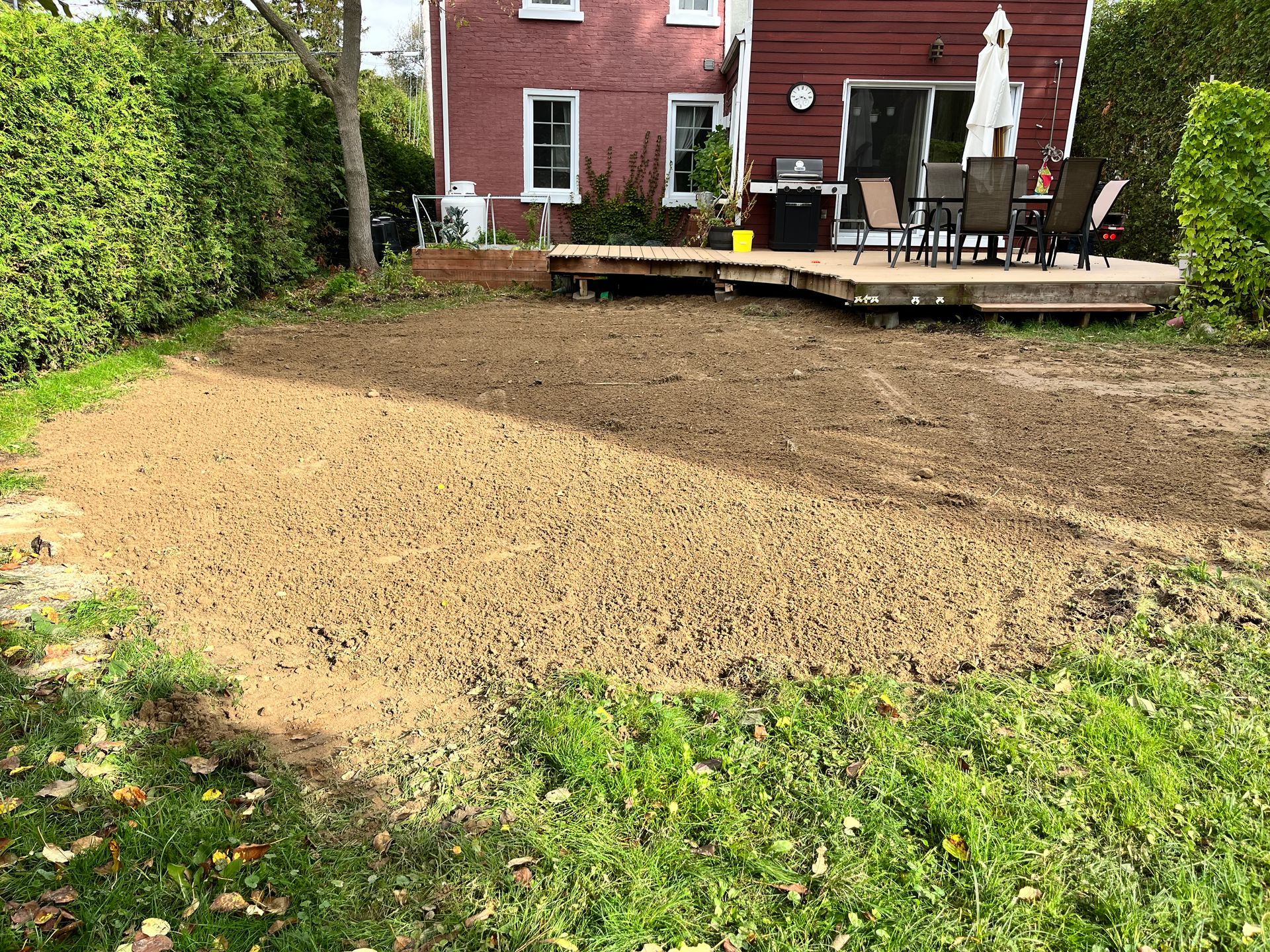 Une cour arrière avec une terrasse et une maison rouge en arrière-plan.