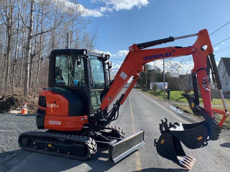 Une petite excavatrice orange et noire est garée sur le bord de la route.