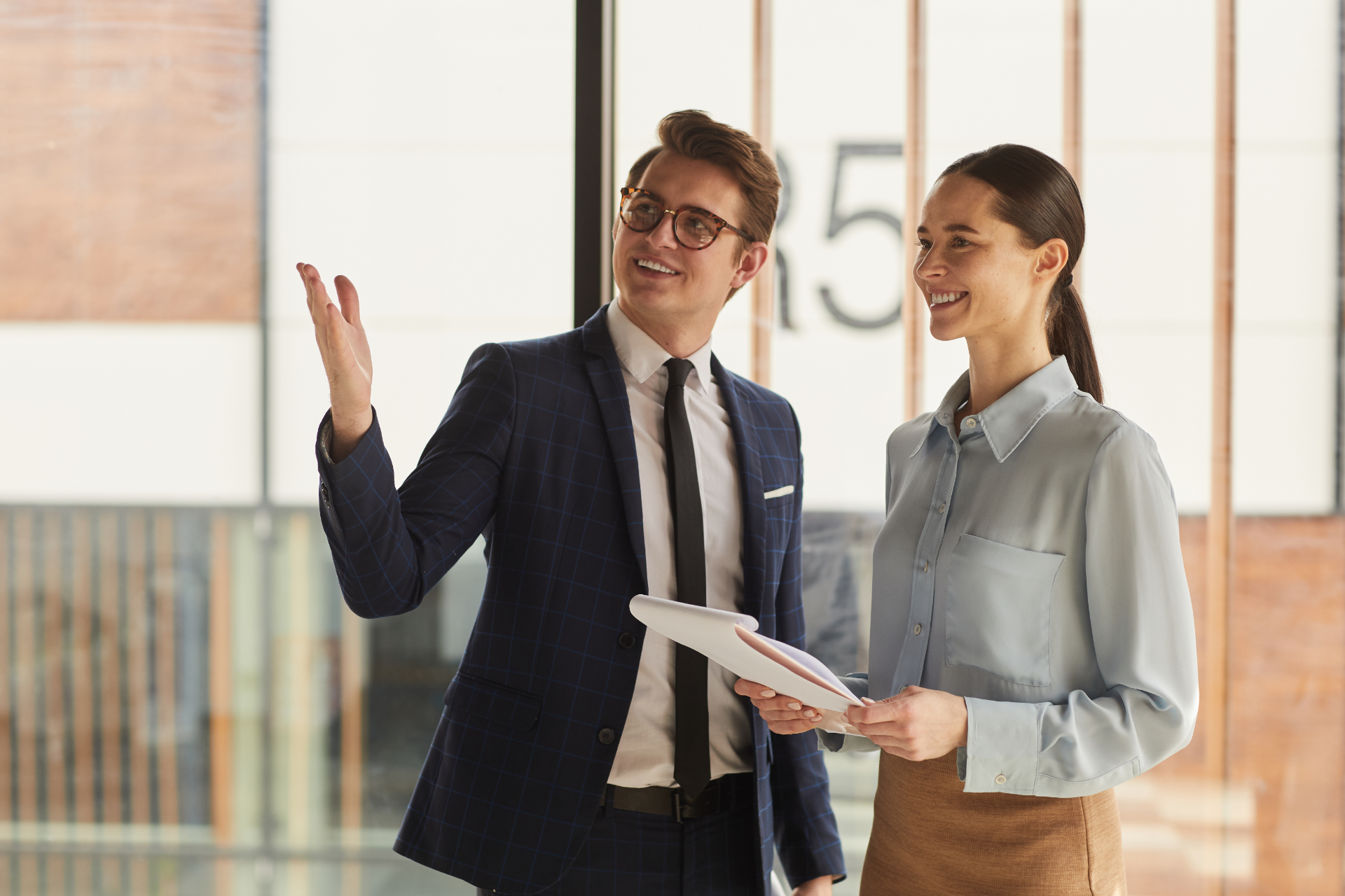 Two professionals discussing a document in a bright office, one gesturing while the other smiles.